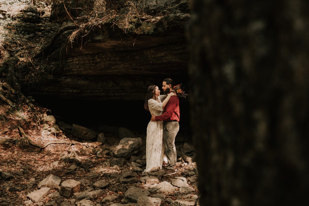 Bride and groom are standing in front of a cave in an embrace.