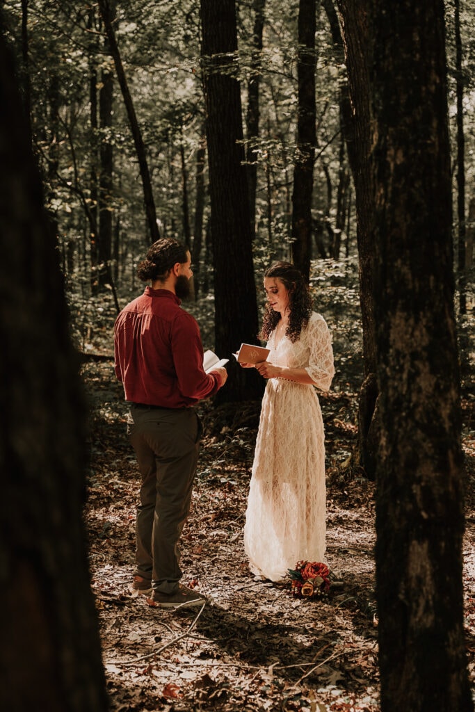 A couple exchanges vows in the middle of the forest while the sun's rays shine down on them during their elopement.