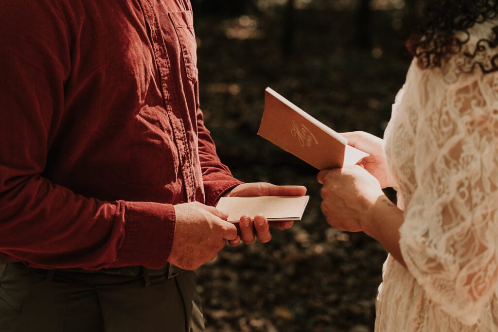 A closeup image of a bride and groom holding vow books, while they read their vows to each other during their outdoor ceremony.