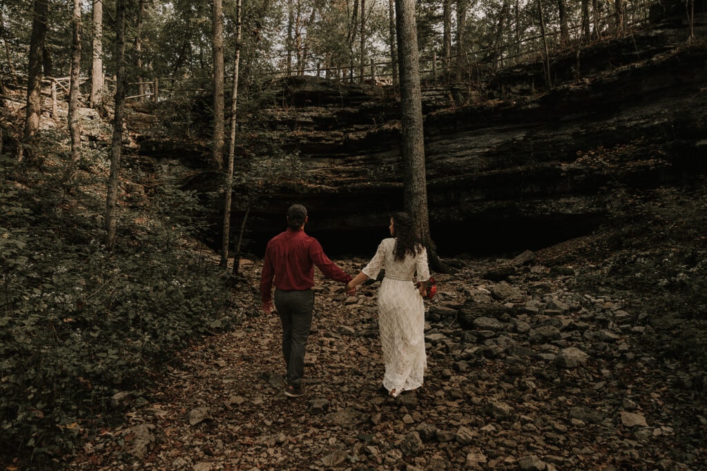 Bride and groom walk hand in hand towards a cave.