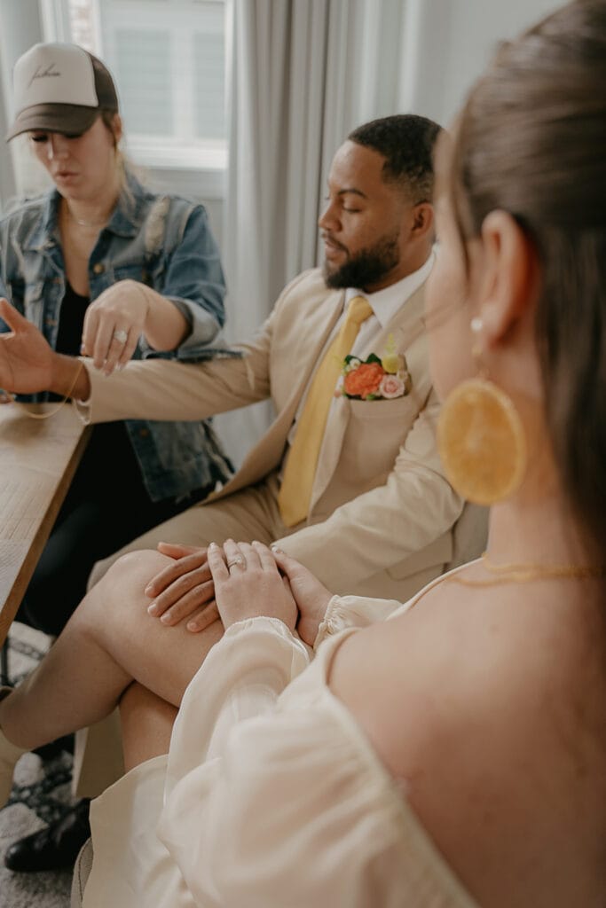 Bride and Groom hold hands while Groom gets fitted with permanent jewelry bracelet during elopement day