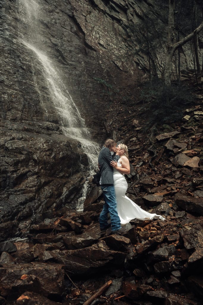 Couple is standing nose to nose in front of waterfall. They are out of focus and the image is focused on the waterfall.