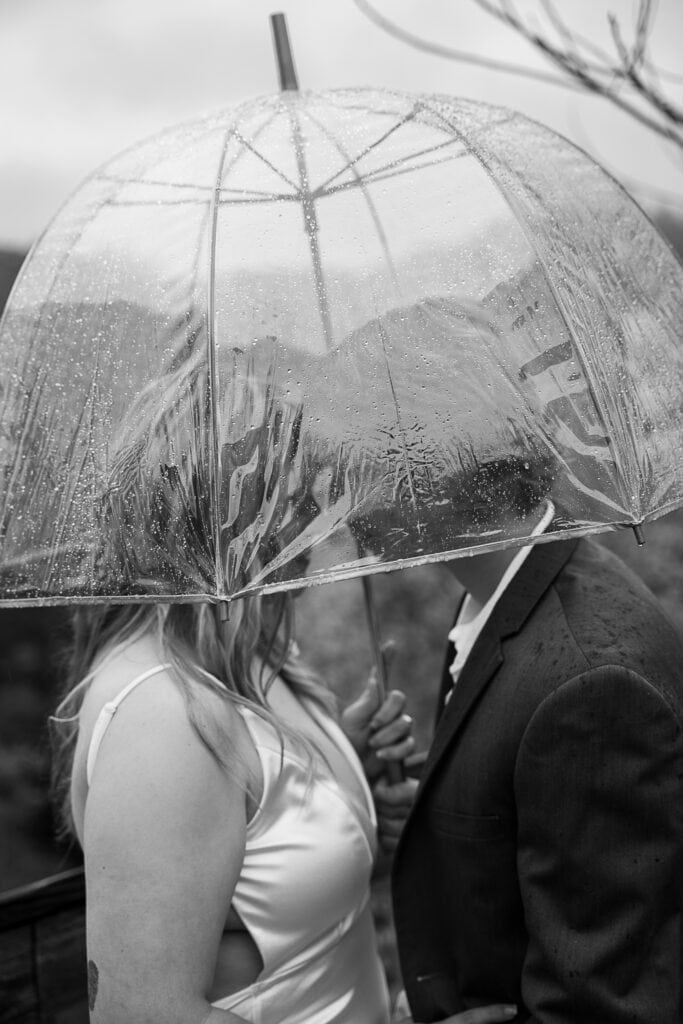 Black and white image of couple enjoying a quiet moment before their elopement. They are under an umbrella.