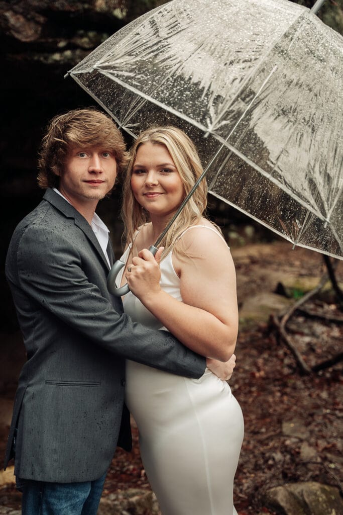 Bride and groom stand off to the side of Foster Falls trailhead. Groom is holding the bride who is holding an umbrella.