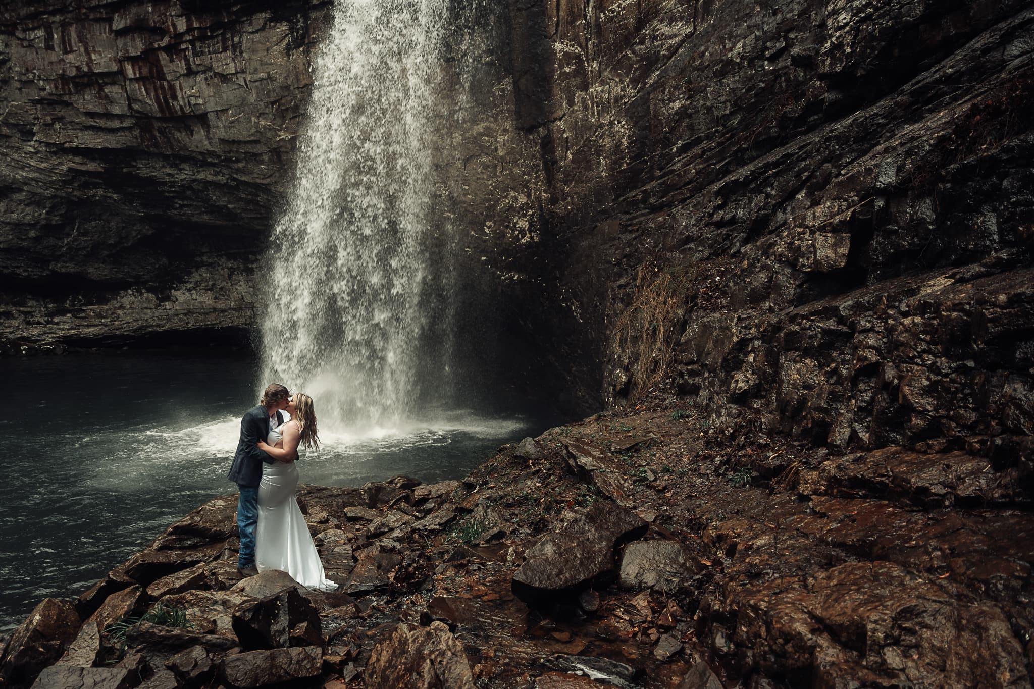 Couple kisses in front of Foster Falls during their rainy Tennessee waterfall elopement ceremony.