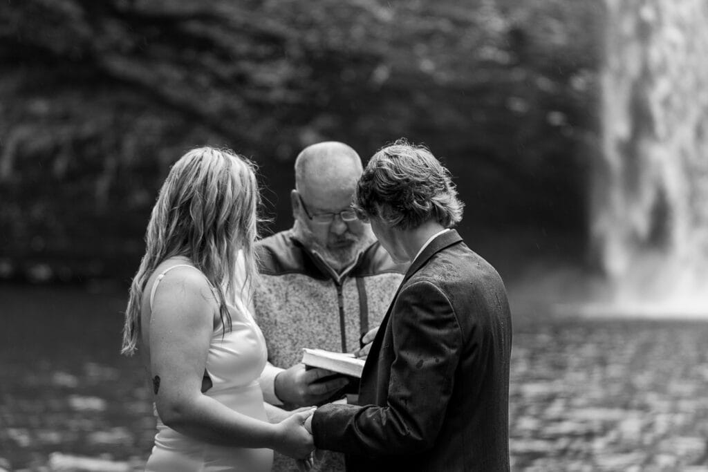 Black and white image of grandpa officiating Ashlyn & Brent's wedding in front of Foster Falls.