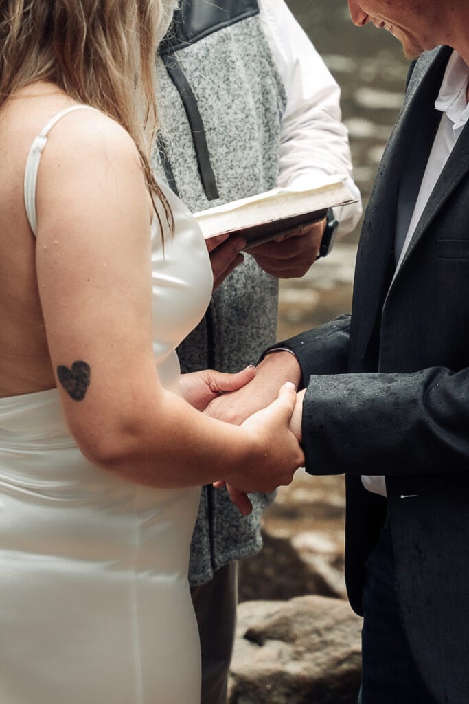 Closeup vertical image of bride holding groom's hand as they say their vows during outdoor ceremony.