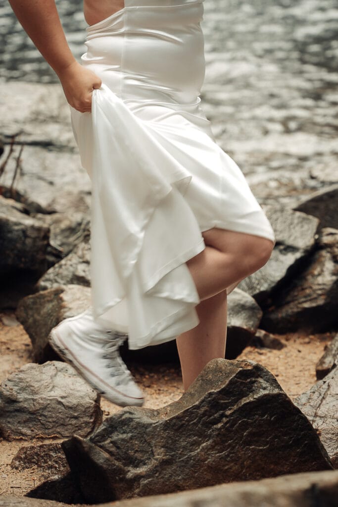 Closeup of Bride's converse tennis shoes as she steps on rocks in sandy area in front of Foster Falls