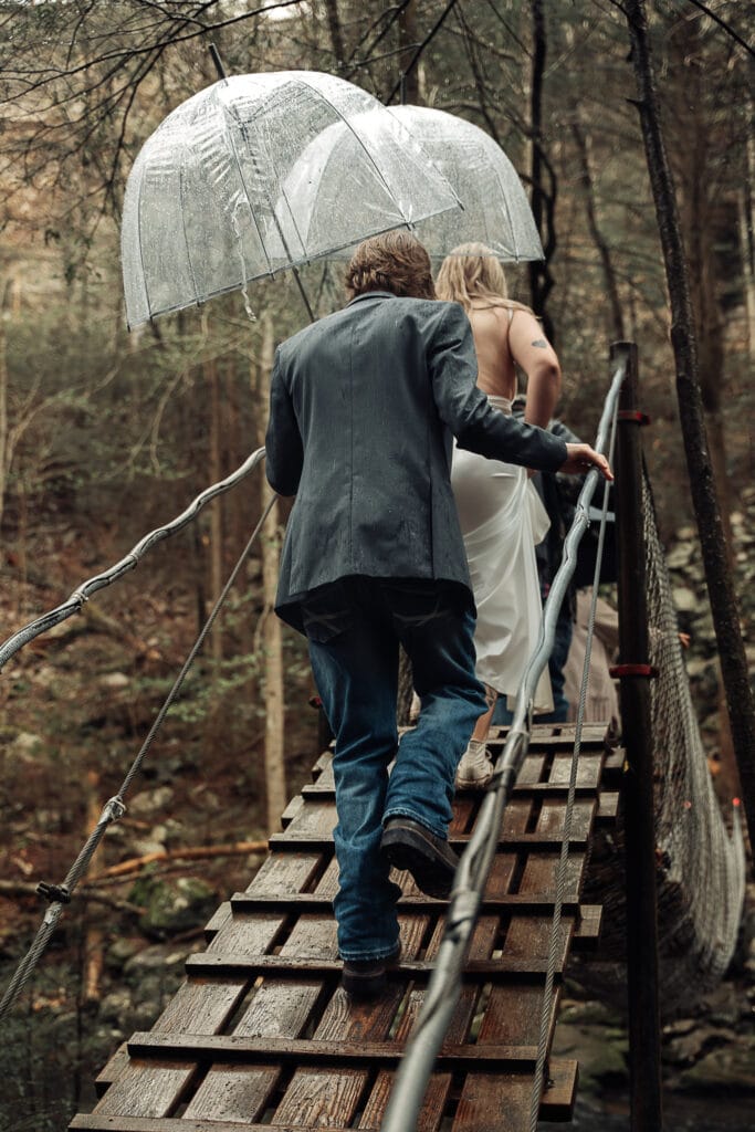 Ashlyn & Brent walk under umbrellas towards the swinging bridge on Foster Falls trail before their wedding begins.