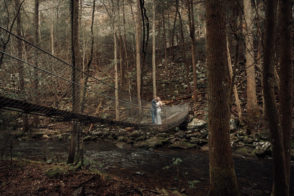 Wide angle swinging bridge near Chattanooga with bride and groom standing in an embrace on it.