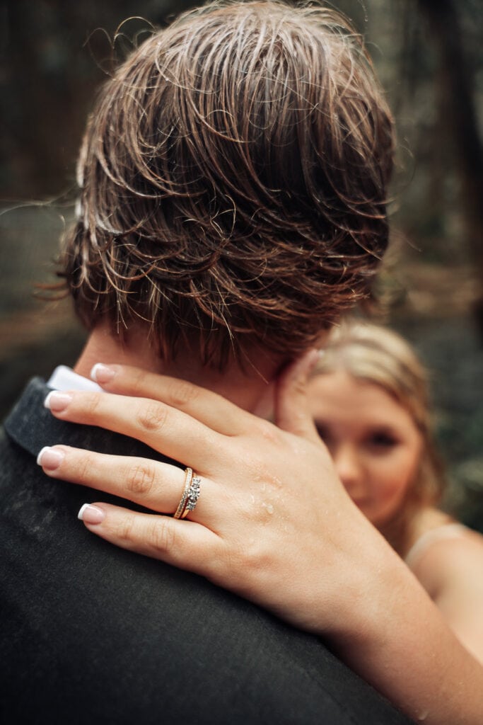 Closeup photo of bride's wedding ring with her hand on the back of groom's neck.