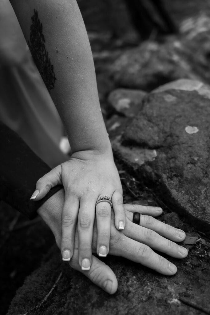 Closeup of couple's hands and wedding rights. Their hands are on top of a mossy rock in the woods.