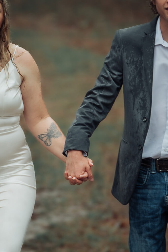 Couple holds hands while walking towards camera. Their faces are cropped out, their hands and muddy trail are center