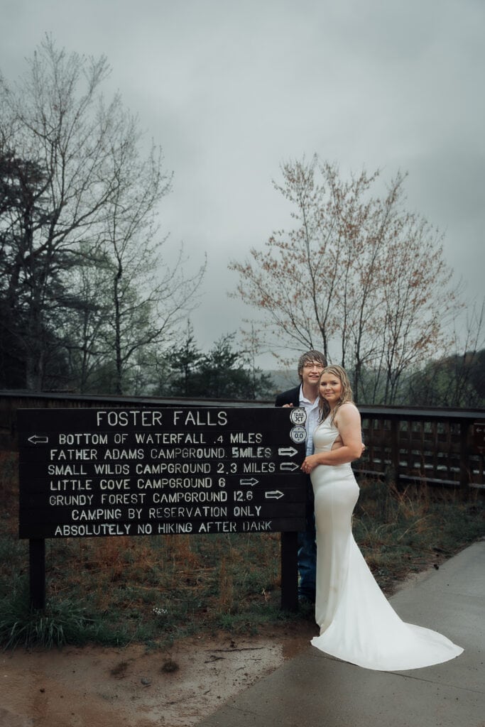 Brent & Ashlyn stand together next to Foster Falls sign before the trail. Skies are cloud and it's pouring rain.