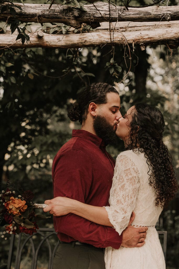 A couple kisses outside in a garden on their wedding day.