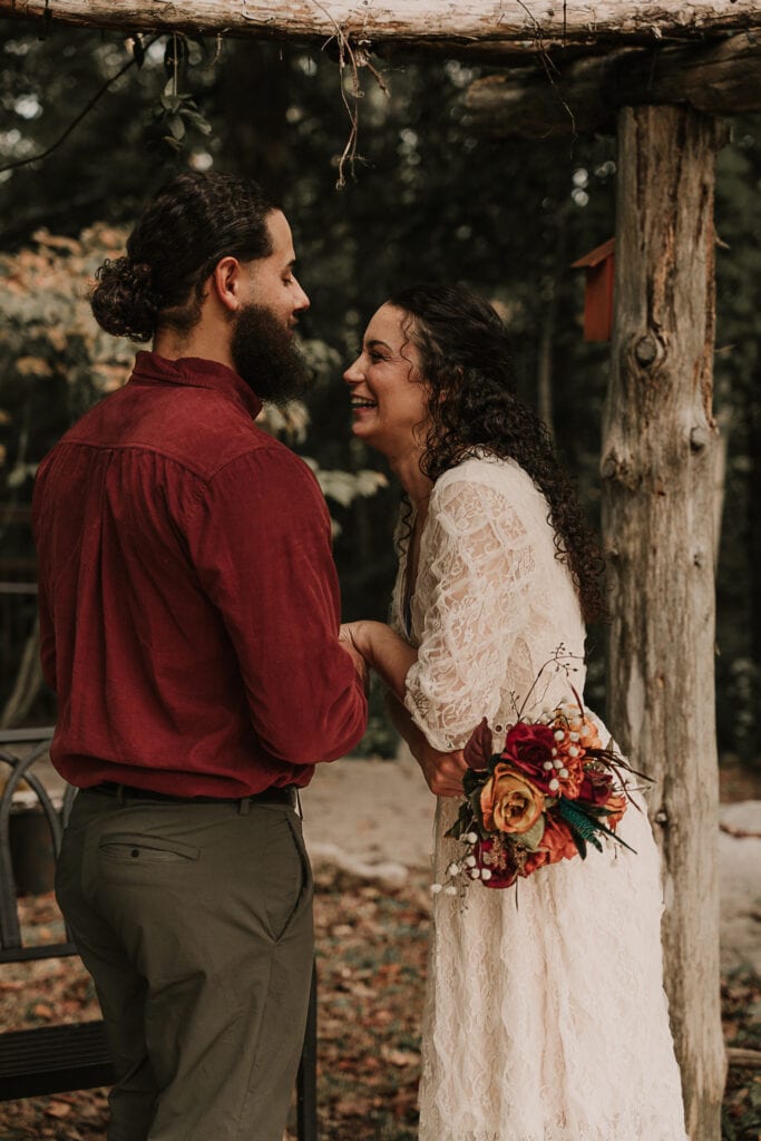 A couple laughs together on their wedding day as they share a private moment in a garden before their ceremony.