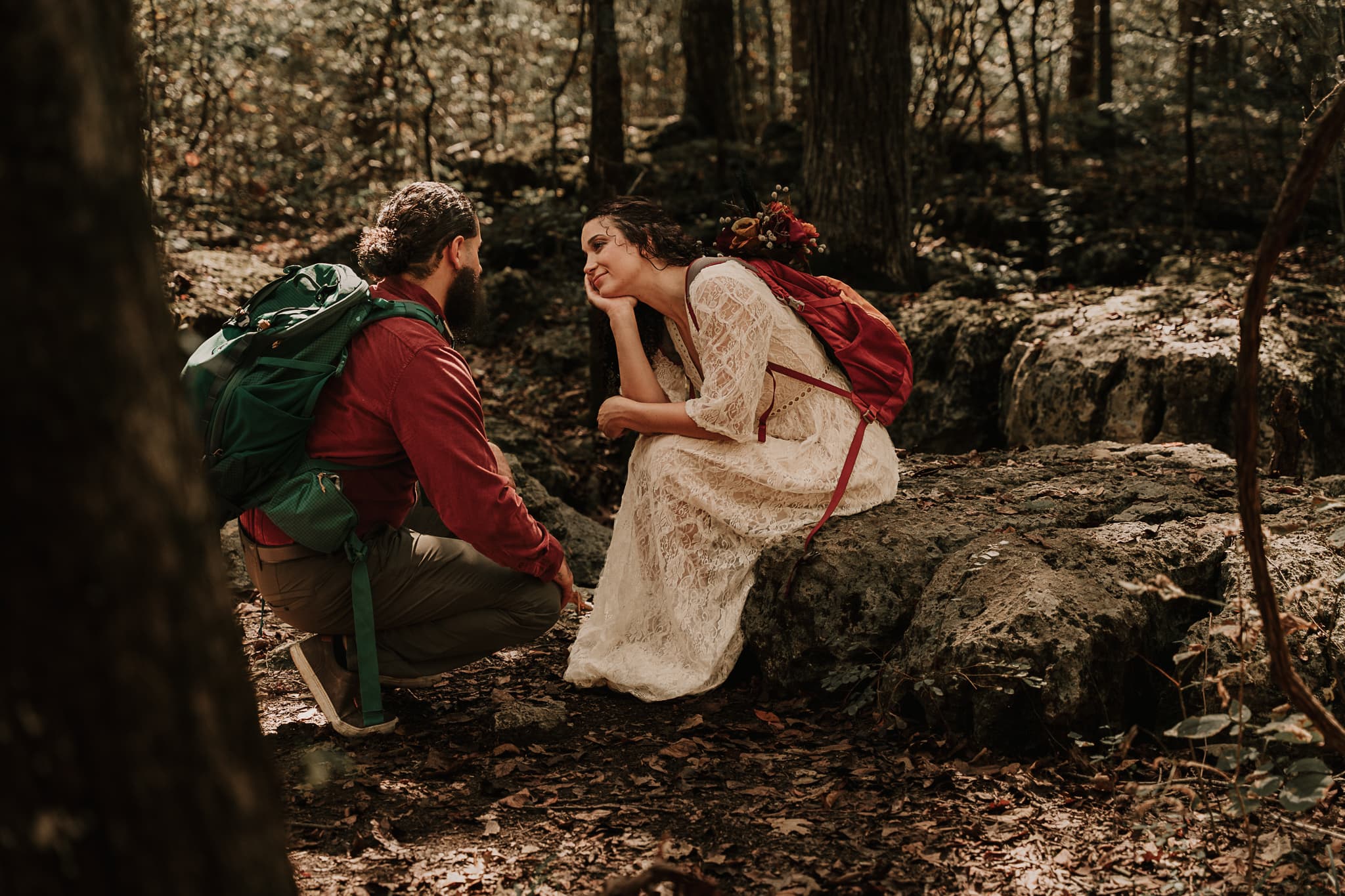 A bride sits on a rock with her head in her hands, talking to the groom, who kneels in front of her, during their hiking elopement.