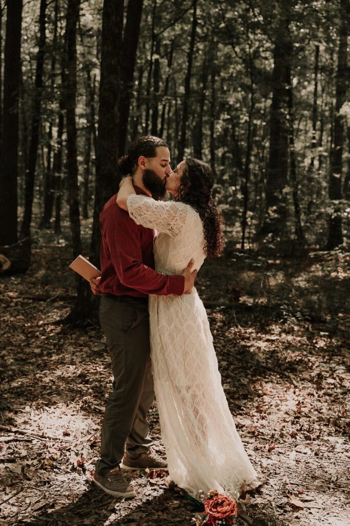 A couple kisses during their outdoor wedding ceremony in the forest.