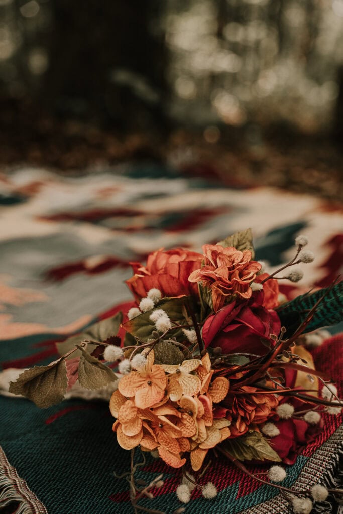 The bridal bouquet sets on a colorful throw blanket outside.