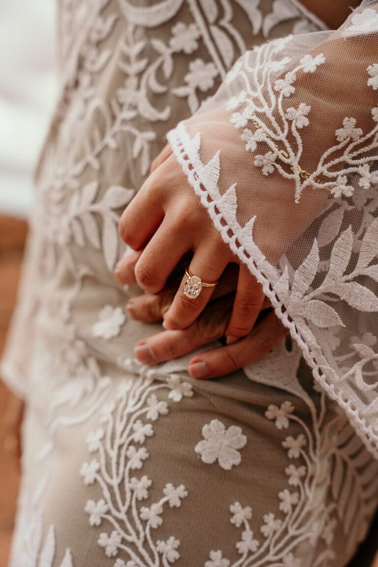 Close up of a bride's hand, showing off her wedding ring against her boho lace wedding dress.