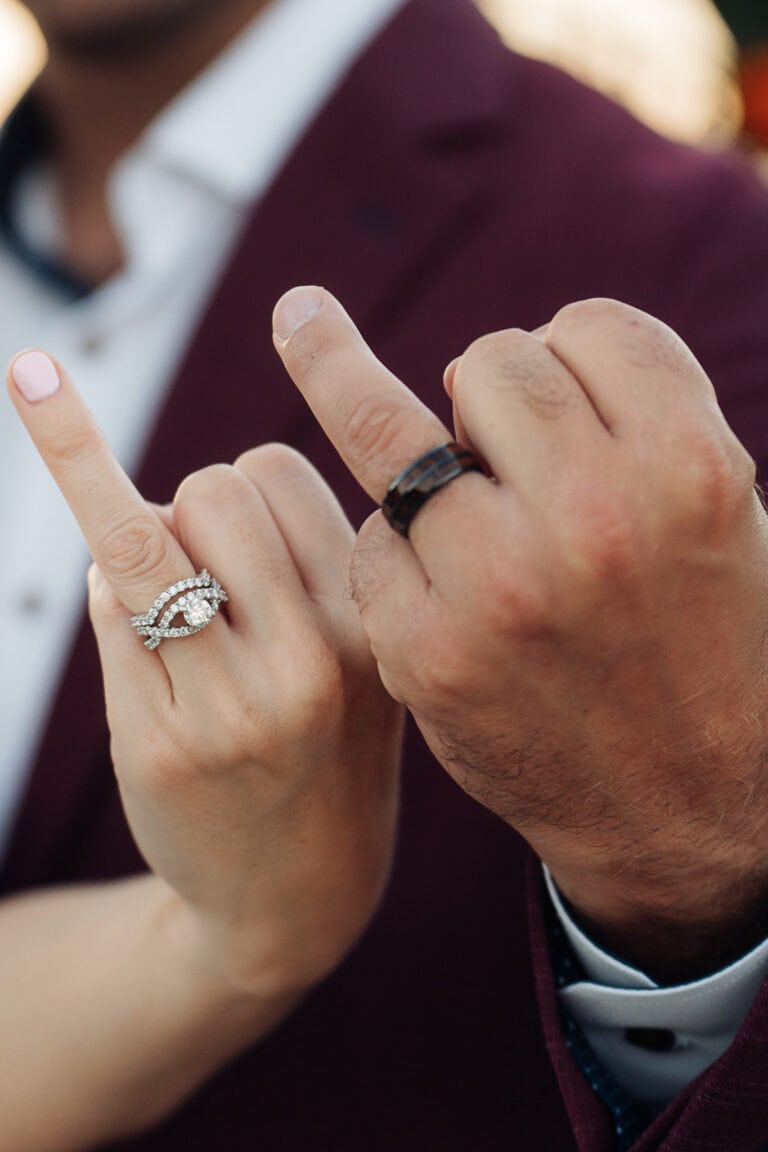 Couple holds ring fingers up towards the camera with their hands next to each other.