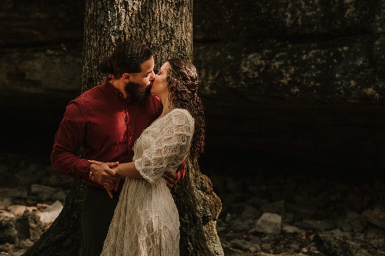 Couple kisses in front of a tree in the forest during their elopement wedding ceremony.