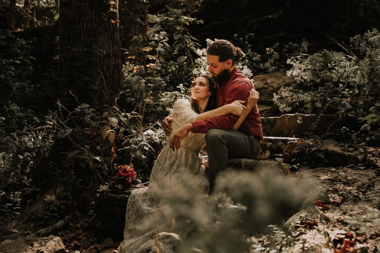 Eloping couple sit on rock steps during their elopement while the sun rays shine down on them through the forest.