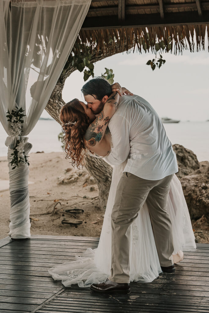 Man dips bride for the kiss at the end of the beach elopement ceremony.