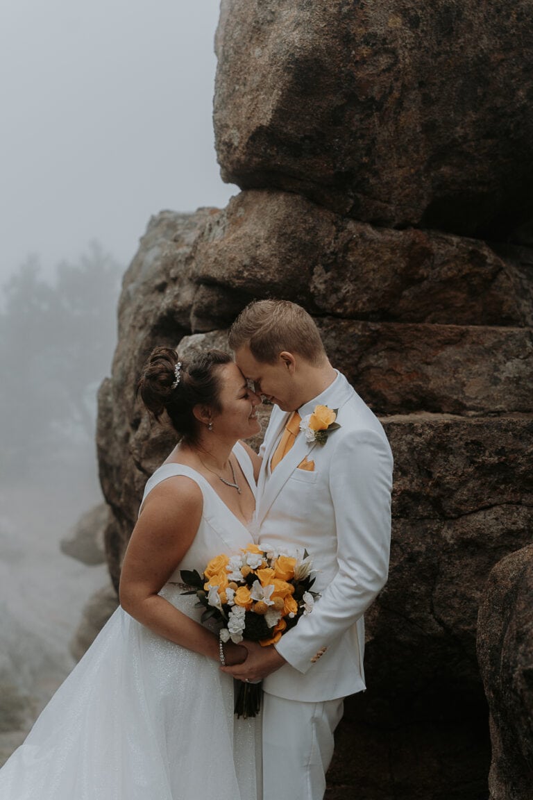 A couple kisses at their elopement on top of Kruger Rock in foggy weather in Estes Park, Colorado.