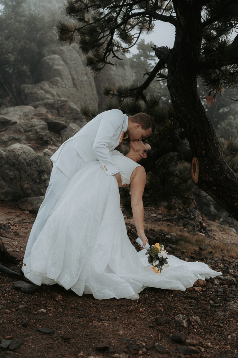 Groom dip kisses bride during their elopement on a trail in Estes Park. It is foggy in the forest.