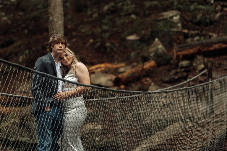 couple in wedding attire stands on swinging bridge in south cumberland state park forest