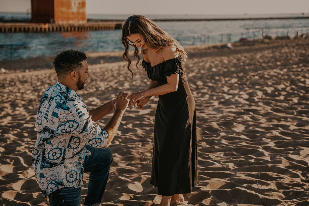 Man proposes to woman on the beach in front of Big Red Lighthouse in Holland Michigan.