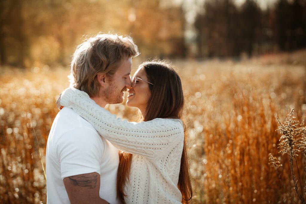 A couple passionately looks into each other's eyes with their arms around each other as they stand in a wheat field at sunrise.