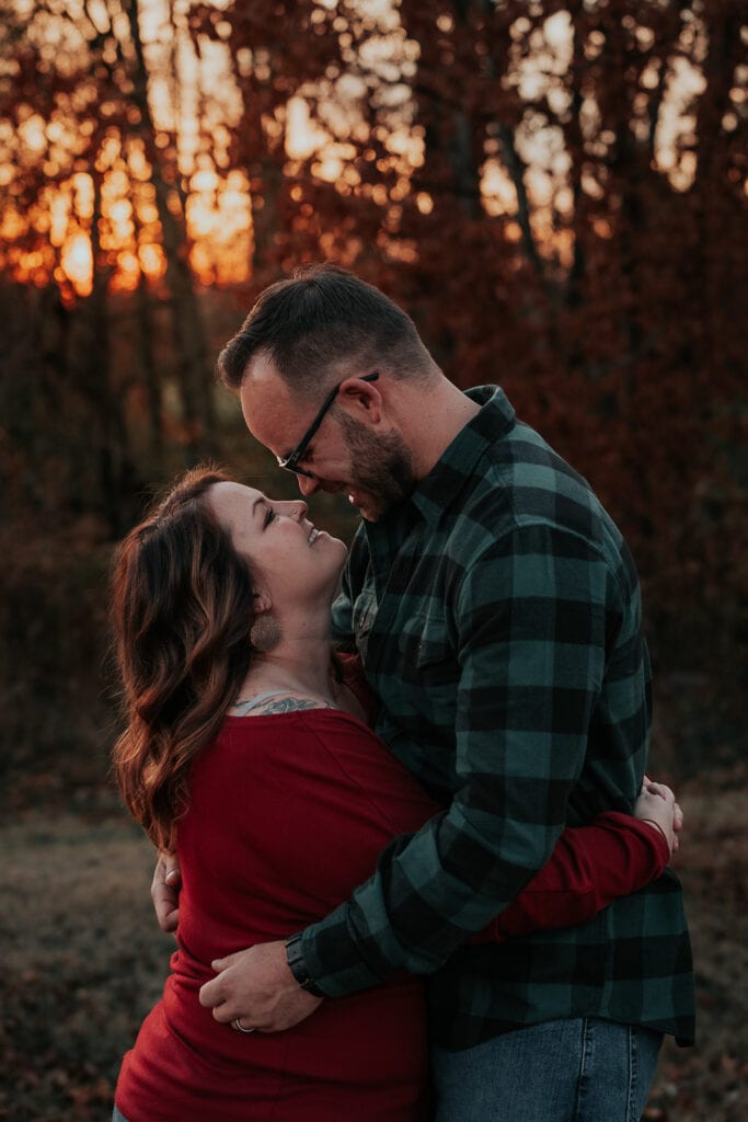 A couple embraces and touches noses in front of an autumn sunset.