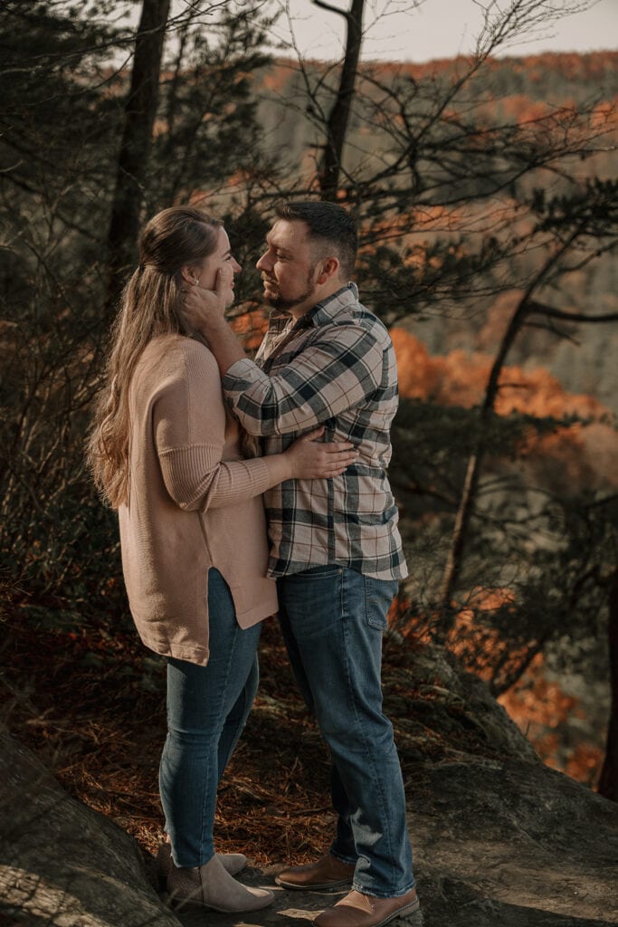 Man and woman stand facing each other outside. Her arms are on his waist and he's lightly touching her face.