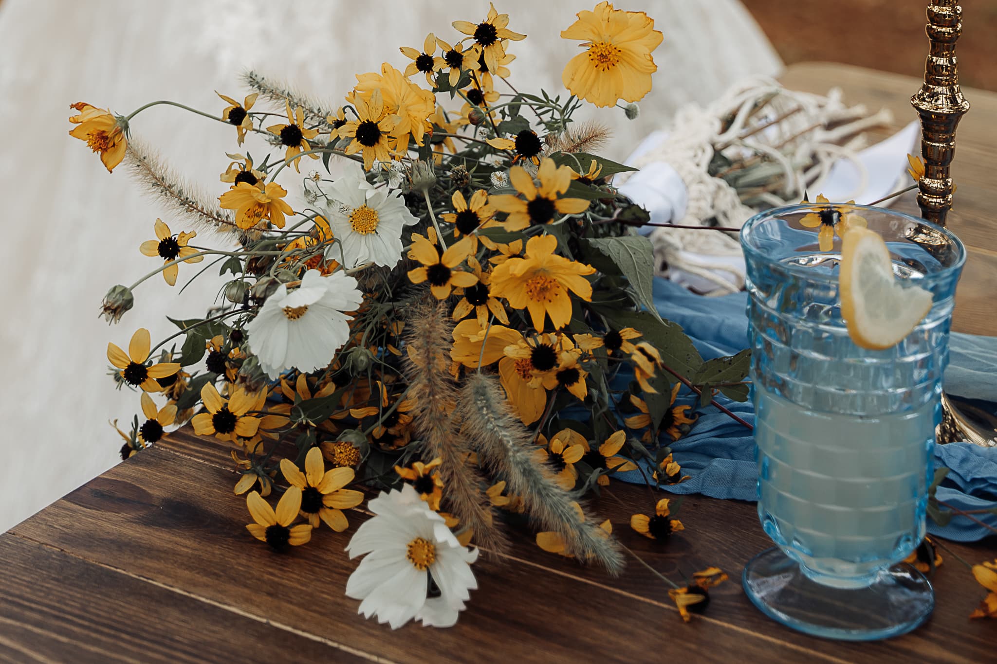 A bouquet of black-eyed susans sits on a table next to a glass of lemmonade.