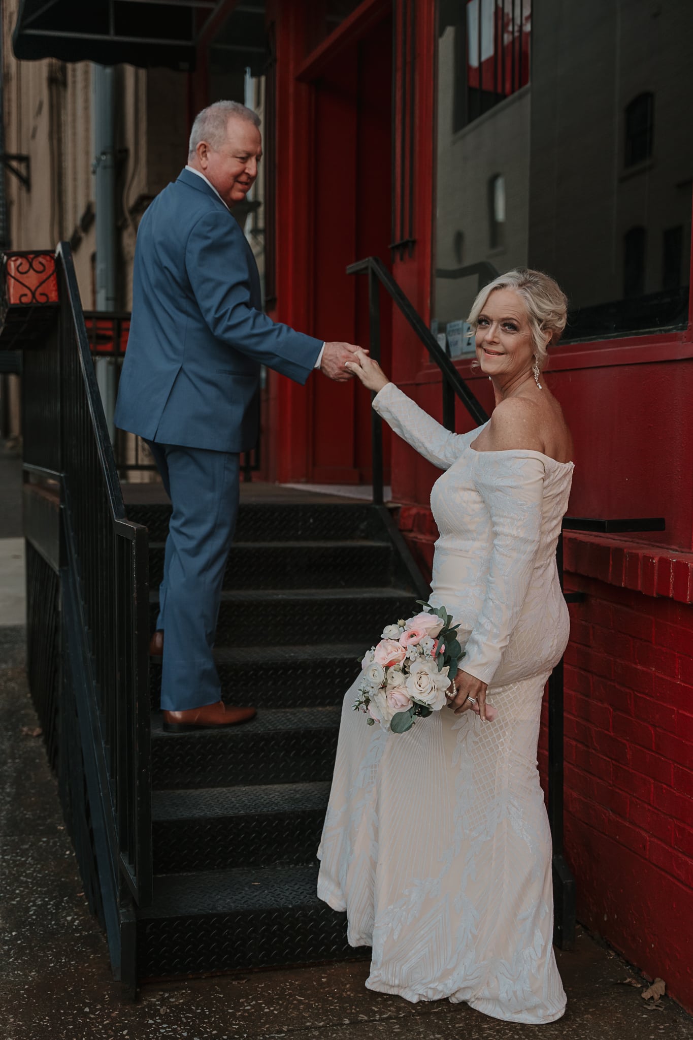 Groom pauses while walking up the stairs to look at his Bride who is looking back at the camera.