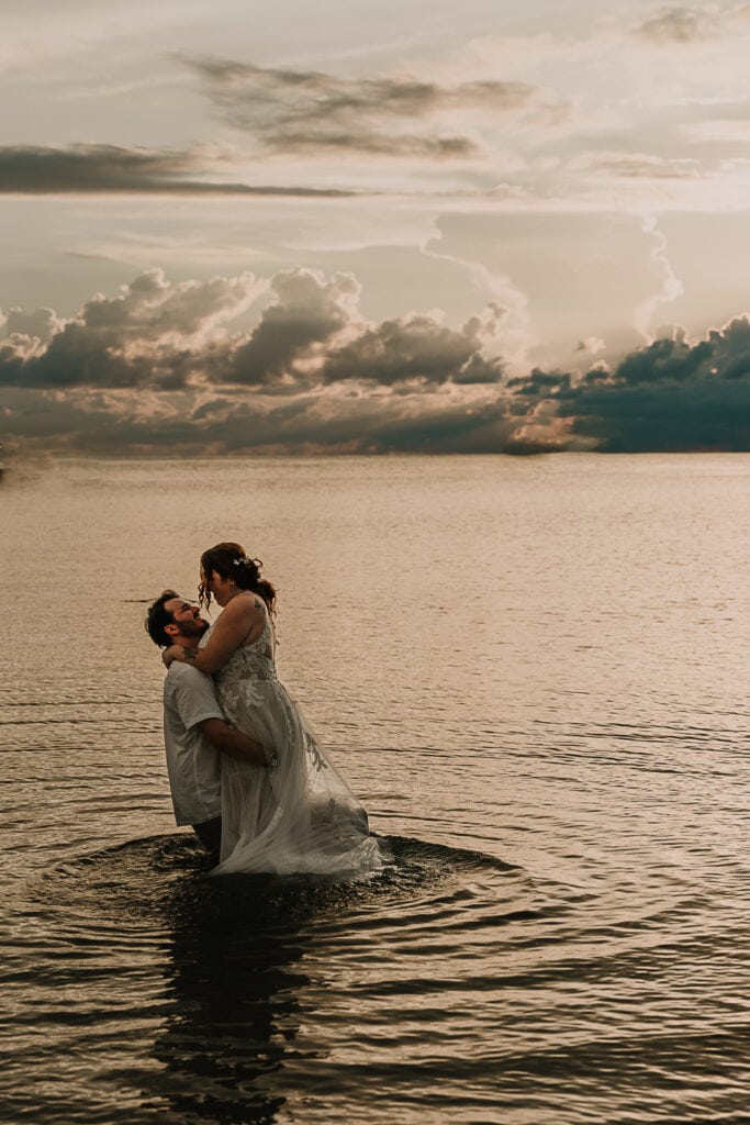 A couple plays in the ocean while wearing their wedding attire.