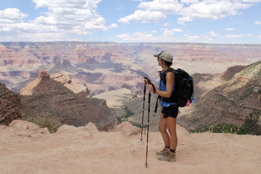 A hiker rests on trekking poles and looks out across the Grand Canyon.