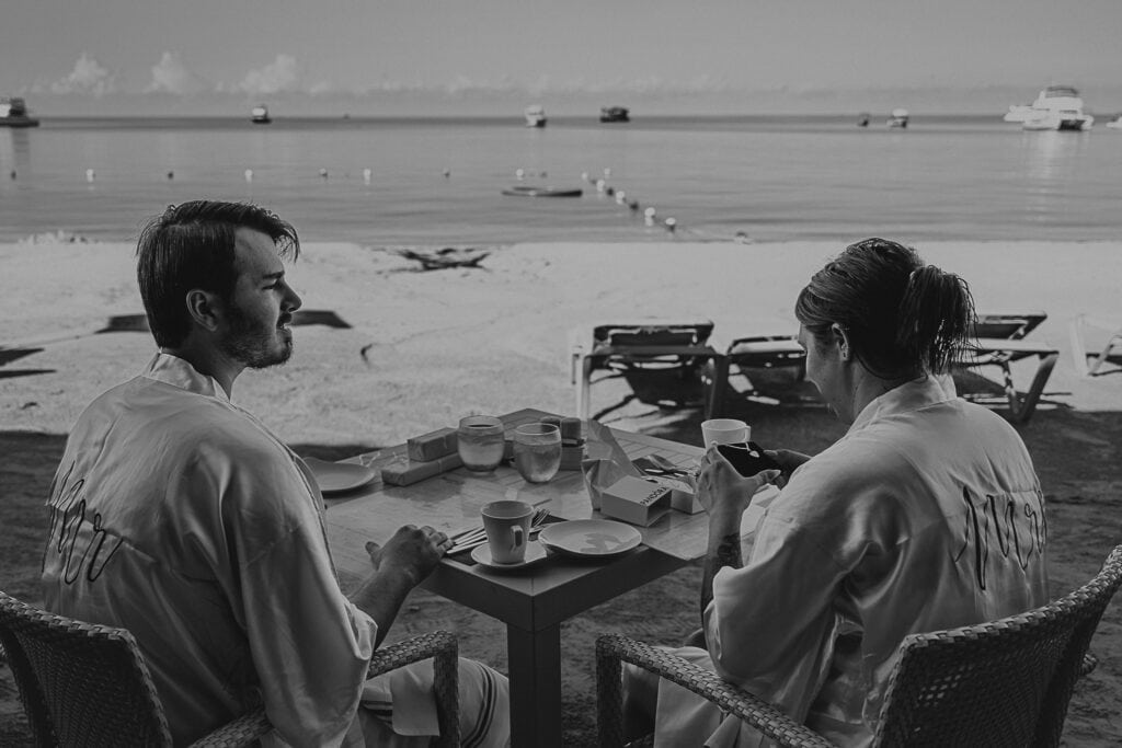 David watches Marissa open the gift he got her. They are sitting on the beach having breakfast.