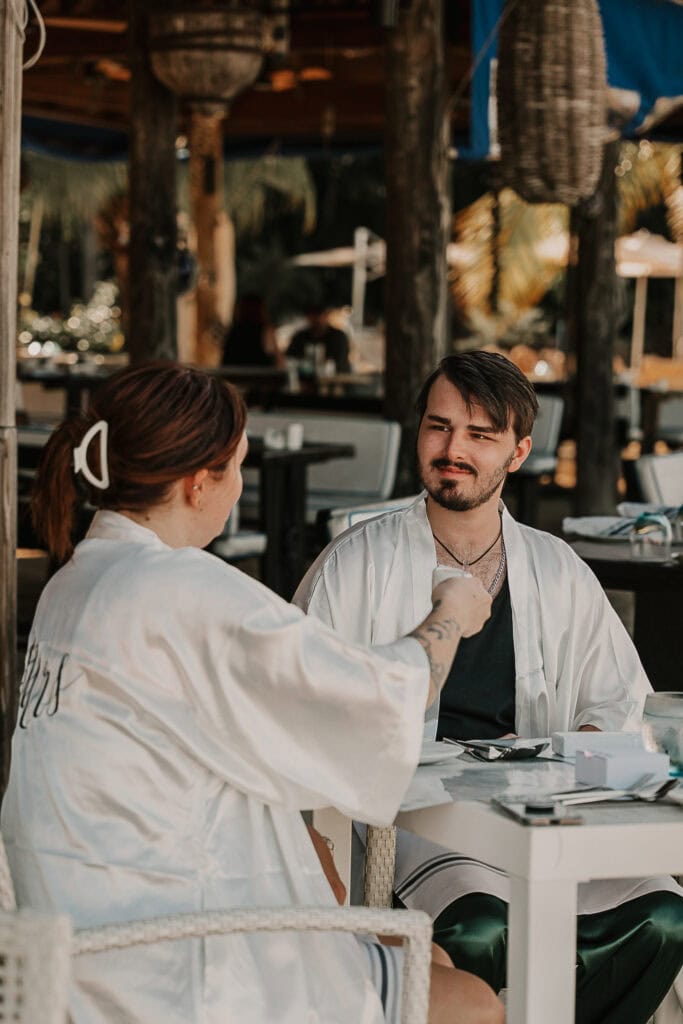 A couple in wedding robes sits at a breakfast table.