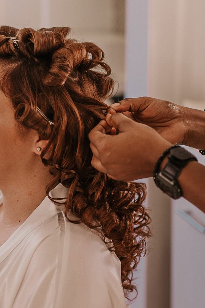 A hair stylist curls a bride's hair.