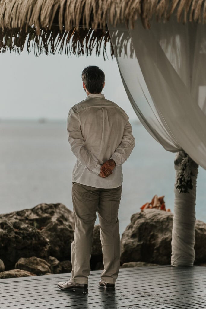 A groom looks at the ocean as he awaits his bride to come down the aisle.