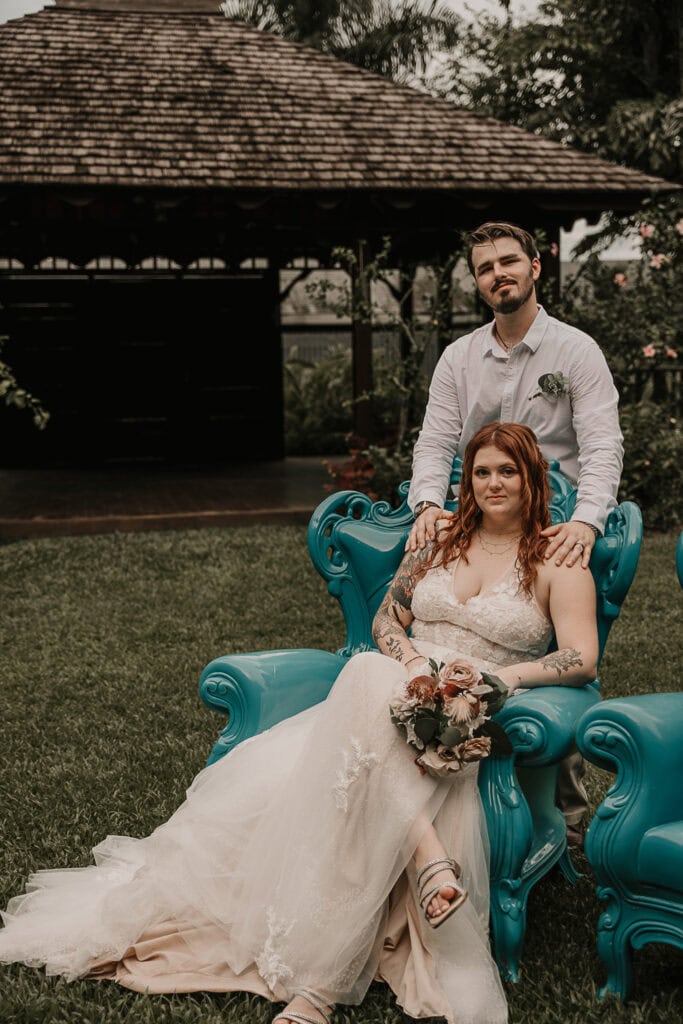 Bride and groom strike an editorial pose in a fancy chair outside.