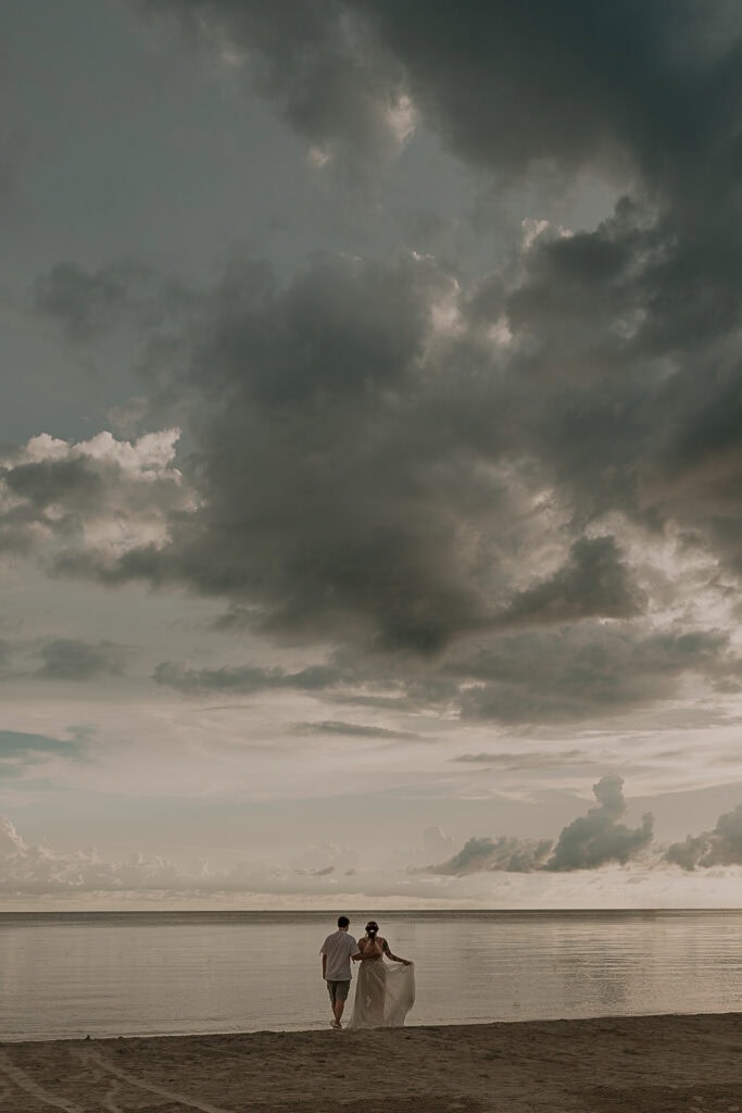 A couple stands on a beach looking out at the ocean after their wedding.