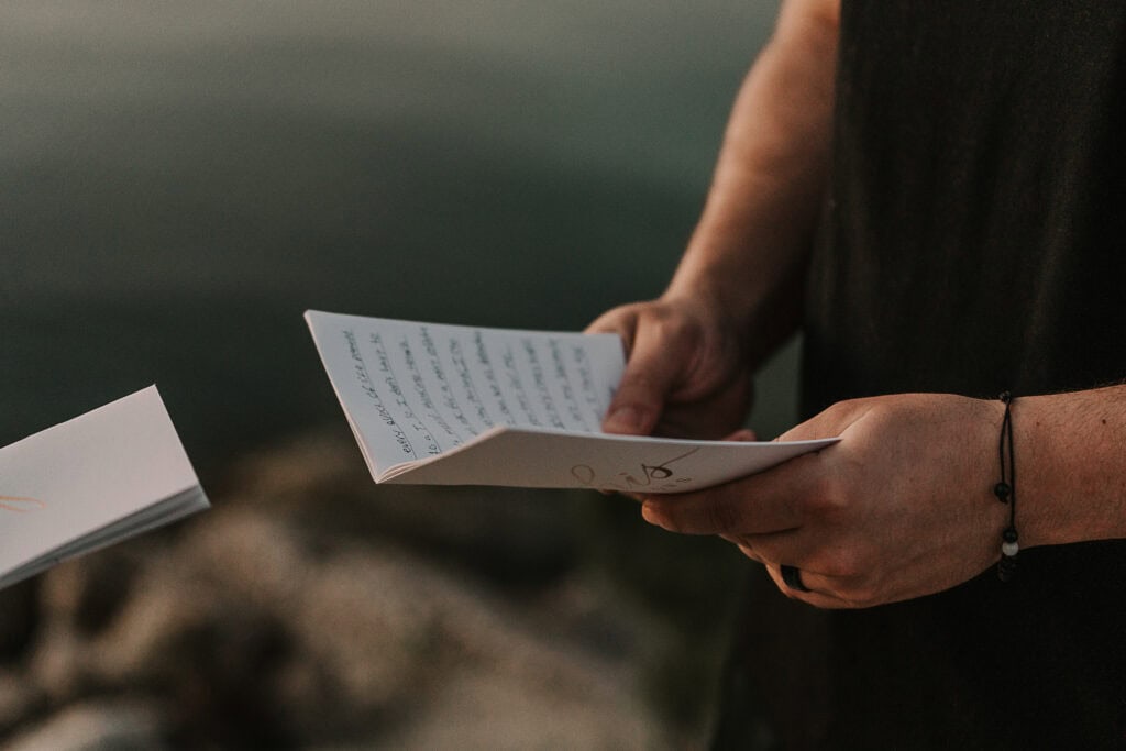 A closeup of a man holding a vow book, filled with handwritten vows.