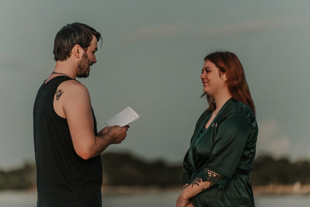 Marissa smiles at David as he reads his vows to her while they're standing on the beach.