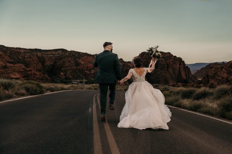 Just married couple runs down the middle of the road in Snow Canyon State Park.