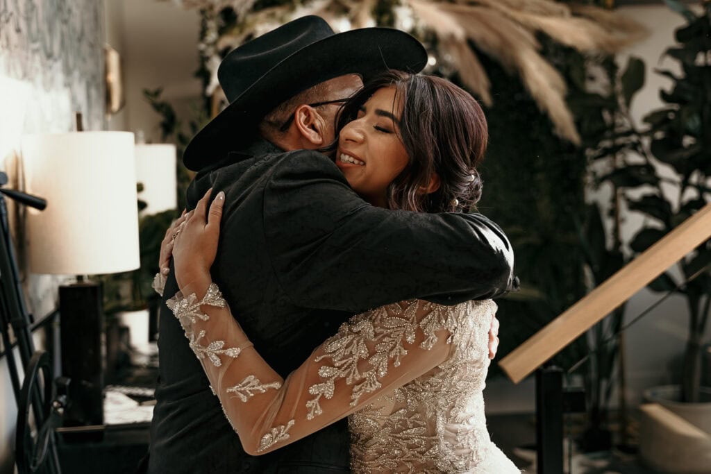 A father in a cowboy hat hugs his daughter during the first look with her in a wedding gown.