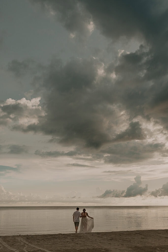 Bride and Groom stands looking out at the ocean during sunset on the beach.